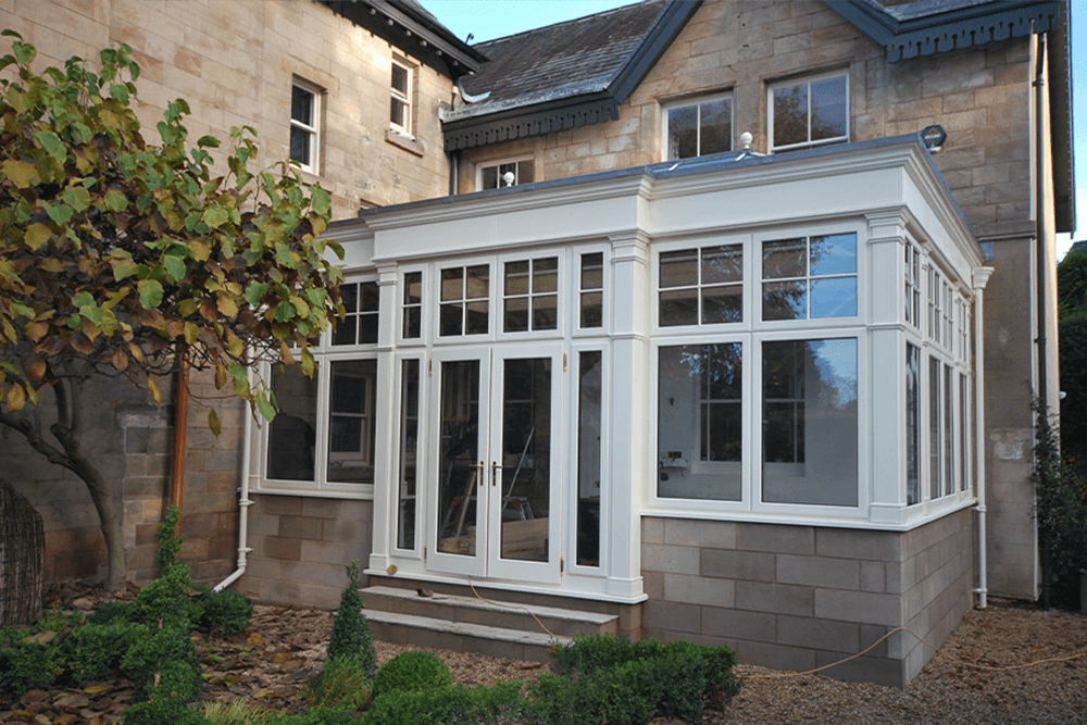 a white orangery with solid roof.